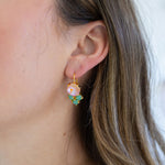 Picture of woman wearing dangle earrings with clear pink stones and three small green stones beneath them.