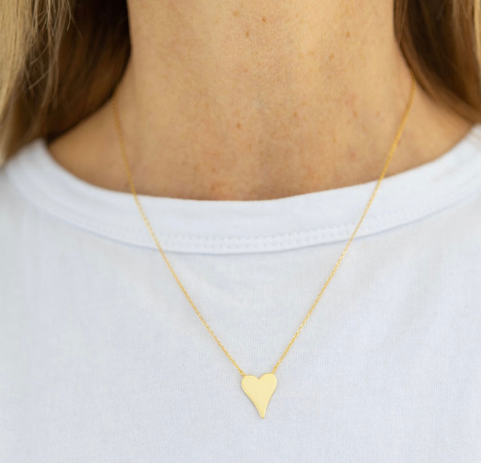 Delicate gold heart necklace worn by a person on a white background
