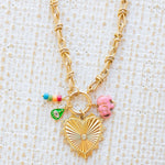 Gold necklace toggle chain with large gold heart pendant with a diamond center.  Three charms attached, one of several multicolored beads, a green evil eye and a pink elephant.