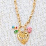 Gold necklace toggle chain with large gold heart pendant with a diamond center.  Three charms attached, one of several multicolored beads, a green evil eye and a pink elephant.