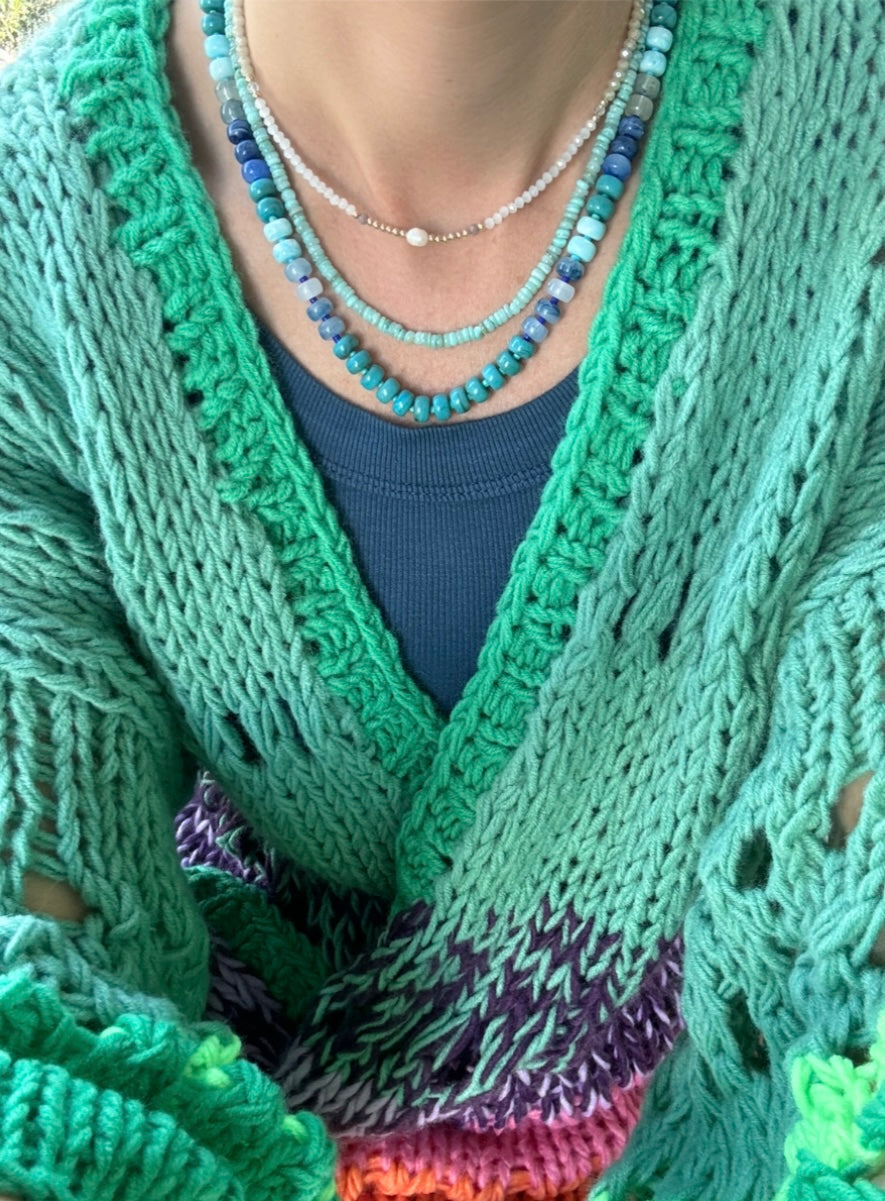 Picture of the front of a woman wearing a set of three bead necklaces. Necklace beads are blues and turquoise