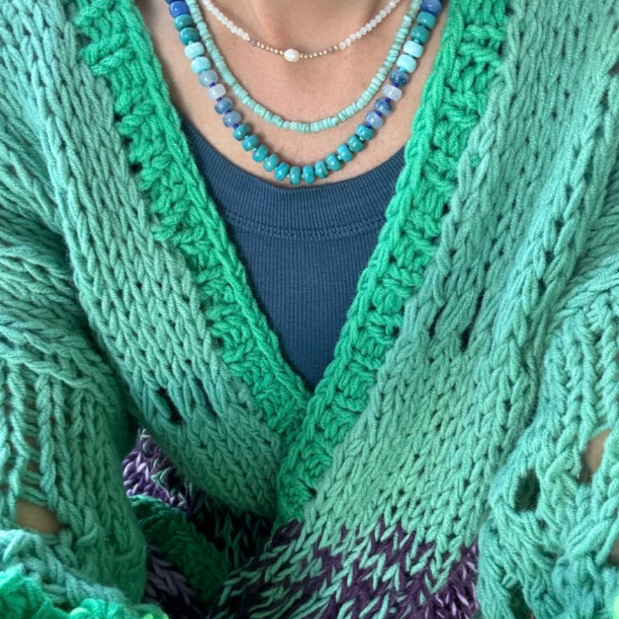 Picture of the front of a woman wearing a set of three bead necklaces. Necklace beads are blues and turquoise