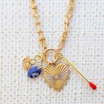 Picture of gold toggle chain with a large gold heart pendant with a diamond at the center. Necklace has three additional charms, a gold and diamond evil eye, a blue marbled bead and a gold matchstick.