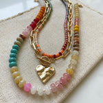 Set of three necklaces made up of small colorful bead necklace, a gold chain link with hammered gold heart pendant and a larger colorful beaded necklace.