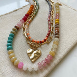 Set of three necklaces made up of small colorful bead necklace, a gold chain link with hammered gold heart pendant and a larger colorful beaded necklace.