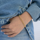 Model's wrist displaying two tiny gold bead bracelets.