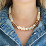 Necklace with gold and beige beads worn by a person in a denim jacket.