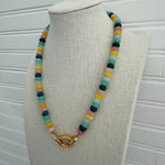 Picture of a necklace made of green, blue, white, yellow and pink beads with a large gold carabiner clasp.
