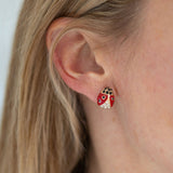 A person wearing ladybug stud earrings with red and black enamel design and a small quartz stone.
