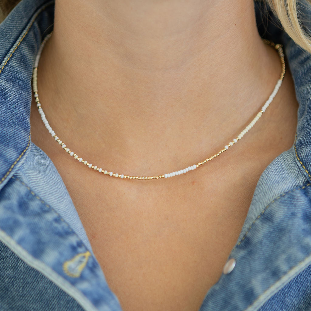 Necklace with small white and gold beads worn by a person wearing a denim top.