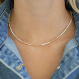Necklace with small white and gold beads worn by a person wearing a denim top.