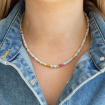 Person wearing a colorful blue and rust beaded necklace with a denim jacket