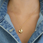 Gold necklace with a gold fortune cookie pendant worn by a person wearing a denim jacket.