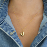 Gold necklace with a gold fortune cookie pendant worn by a person wearing a denim jacket.