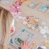 People working on jewelry-making projects at a table with beads and tools.