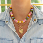 Model wearing chunky multicolored bead necklace stacked with a front clasping gold toggle chain necklace with heart pendant