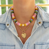 Model wearing chunky multicolored bead necklace stacked with a front clasping gold toggle chain necklace with heart pendant