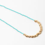 Blue bead necklace with gold beads at it's center.