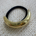Gold hair tie holder with black hair tie on a textured white background