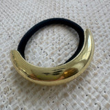 Gold hair tie holder with black hair tie on a textured white background