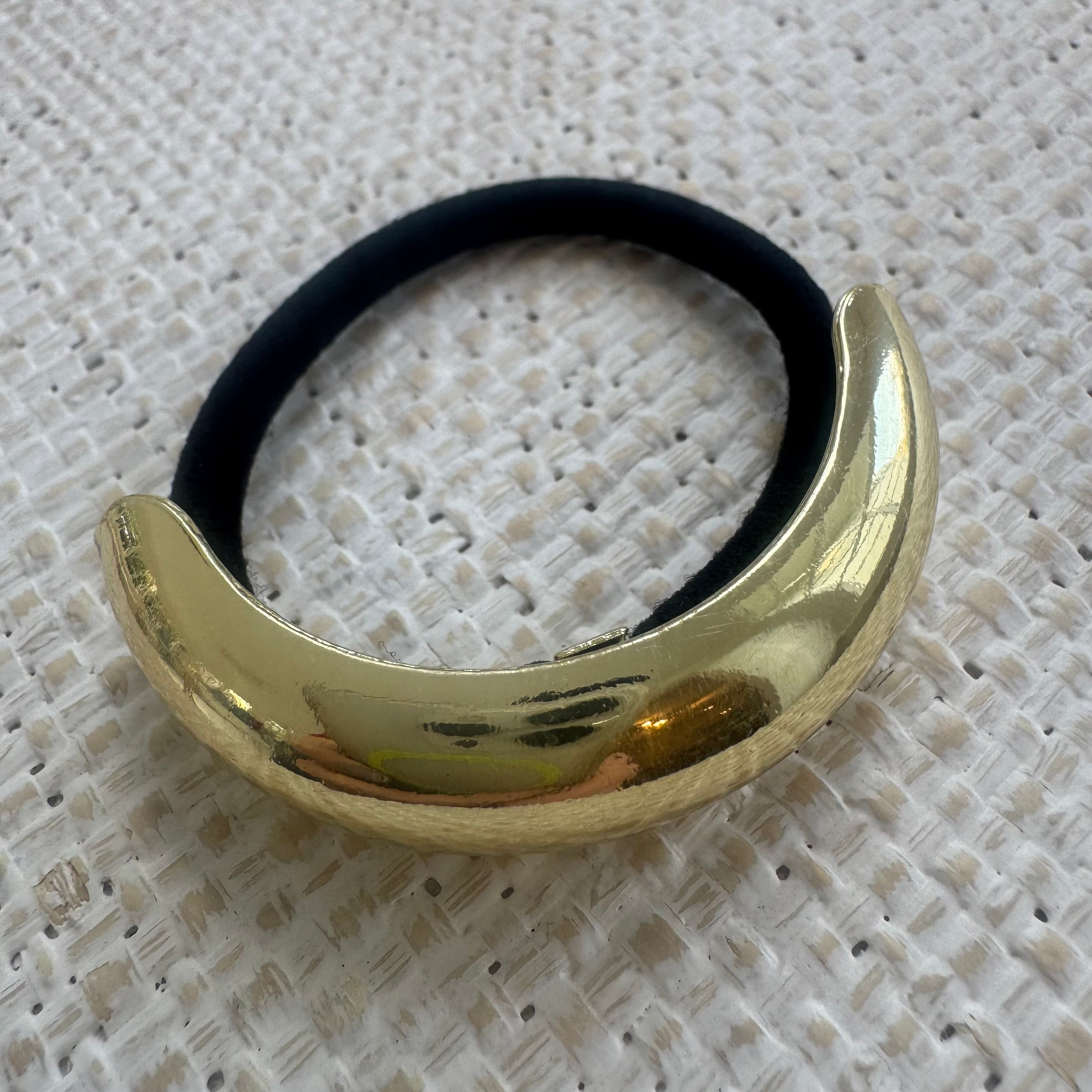Gold hair tie holder with black hair tie on a textured white background