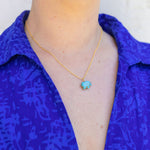 Woman wearing a gold chain necklace with a turquoise blue/brown stone attached to it