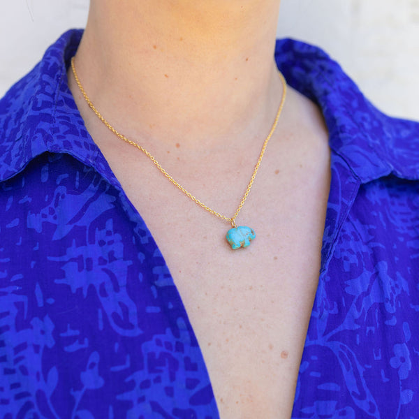 Woman wearing a gold chain necklace with a turquoise blue/brown stone attached to it