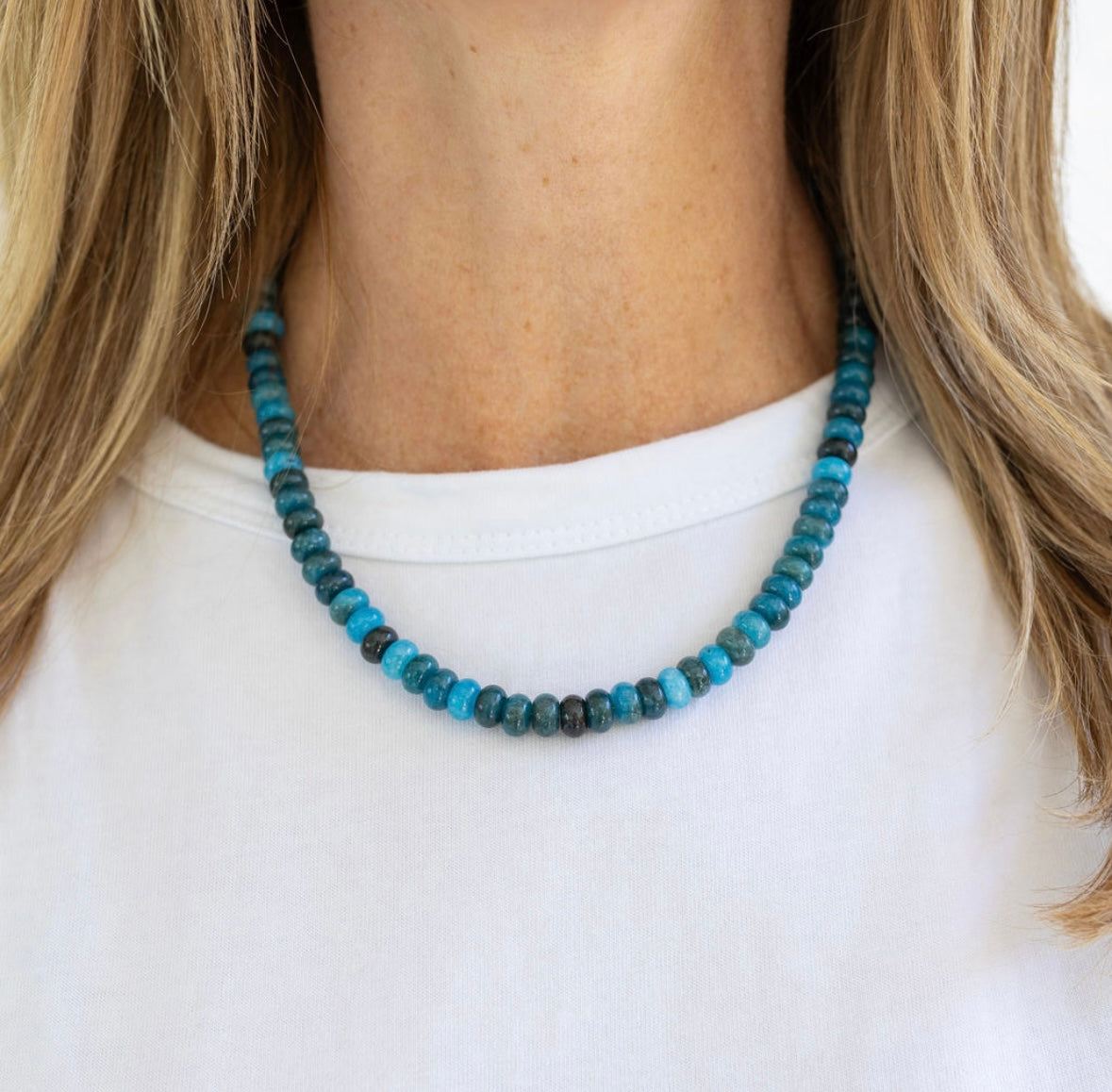 Necklace with blue and black beads worn by a person on a white background