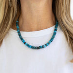 Necklace with blue and black beads worn by a person on a white background