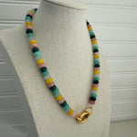 Picture of a necklace made of green, blue, white, yellow and pink beads with a large gold carabiner clasp.