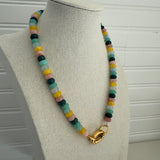 Picture of a necklace made of green, blue, white, yellow and pink beads with a large gold carabiner clasp.