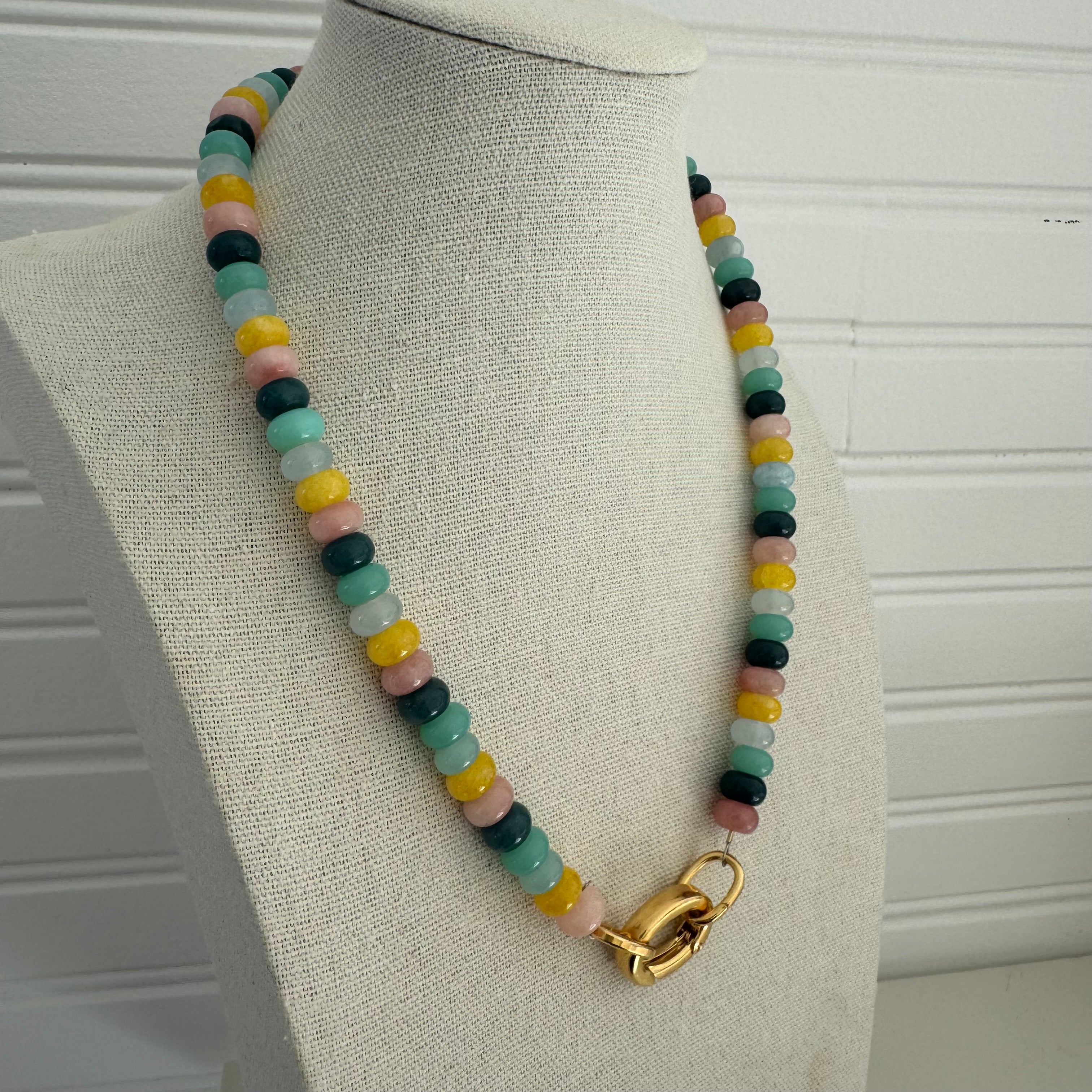 Picture of a necklace made of green, blue, white, yellow and pink beads with a large gold carabiner clasp.