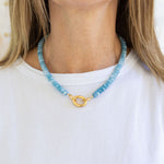 Blue beaded necklace with a gold clasp worn by a person on a white background