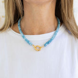 Blue beaded necklace with a gold clasp worn by a person on a white background