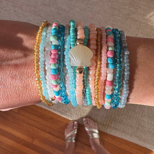Picture of a woman's wrist wearing 16 different bracelets in Beach themed colors.  Bracelets are shades o white, corals, pinks, blues and amber.