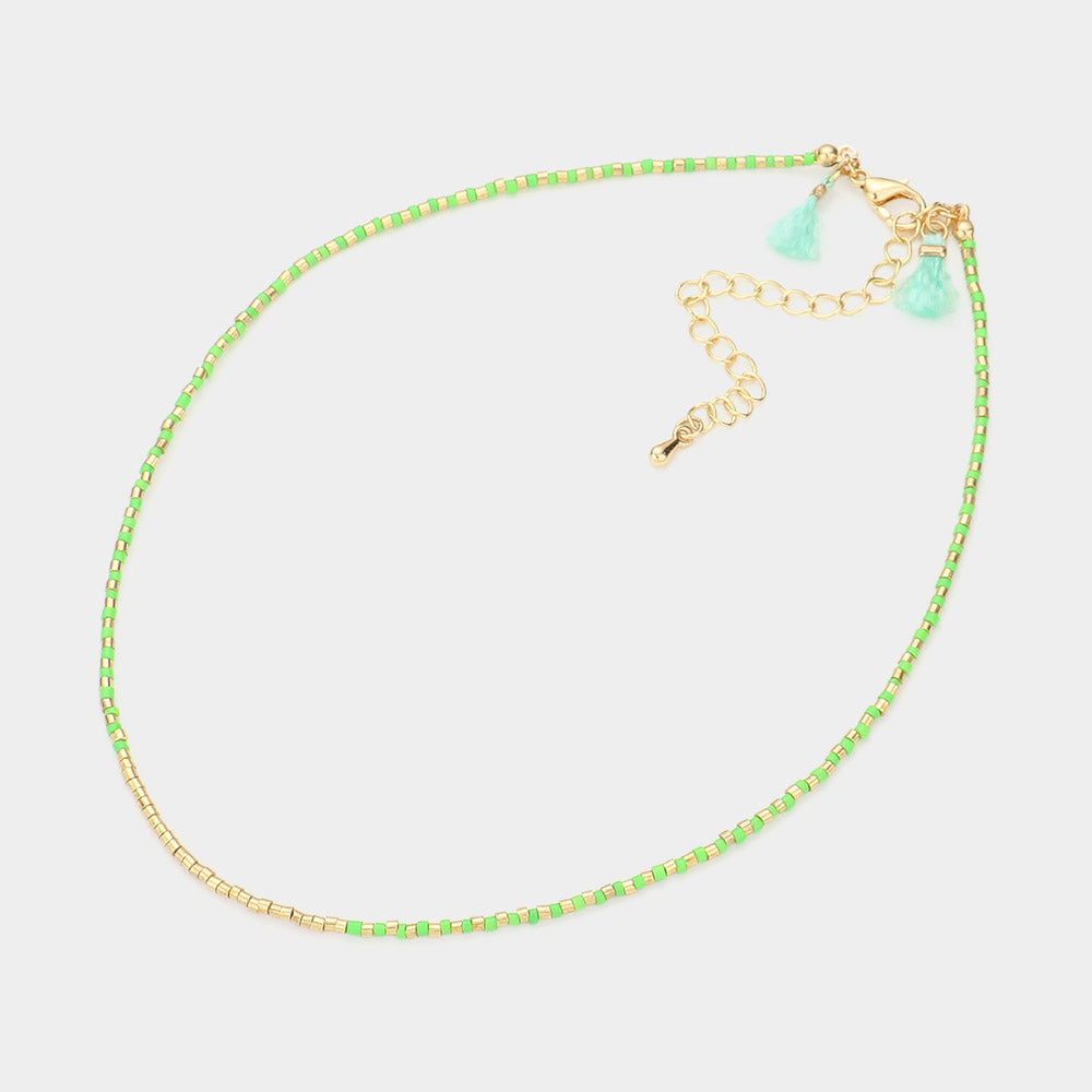 Necklace with green and gold beads and gold chain on a light gray background
