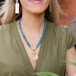 Picture of model wearing a a turquoise beaded necklace with a chunky gold link and large gold heart shaped pendant with a diamond at it's center.