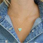 Gold necklace with a turquoise heart pendant worn by a person in a denim jacket.