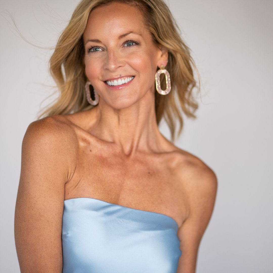 Woman wearing a strapless light blue dress with large gold hoop earrings against a plain background
