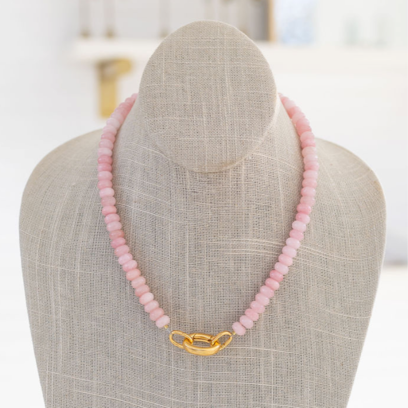 A pink gemstone necklace with a gold carabiner clasp on a mannequin bust.