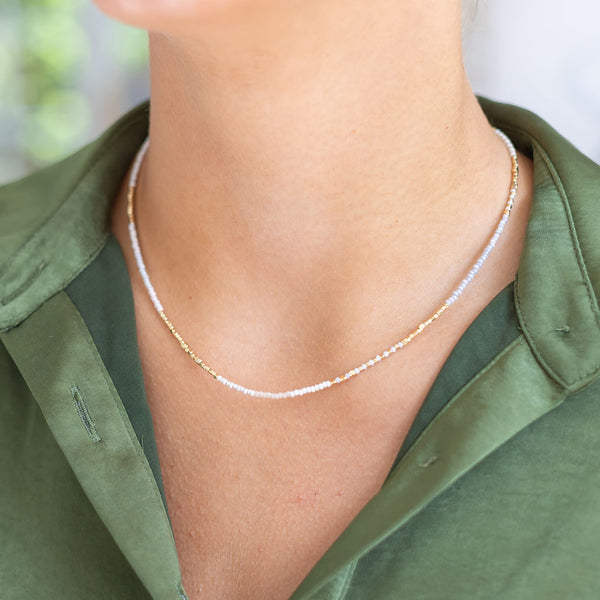 Woman wearing a thin gold/white beaded short necklace