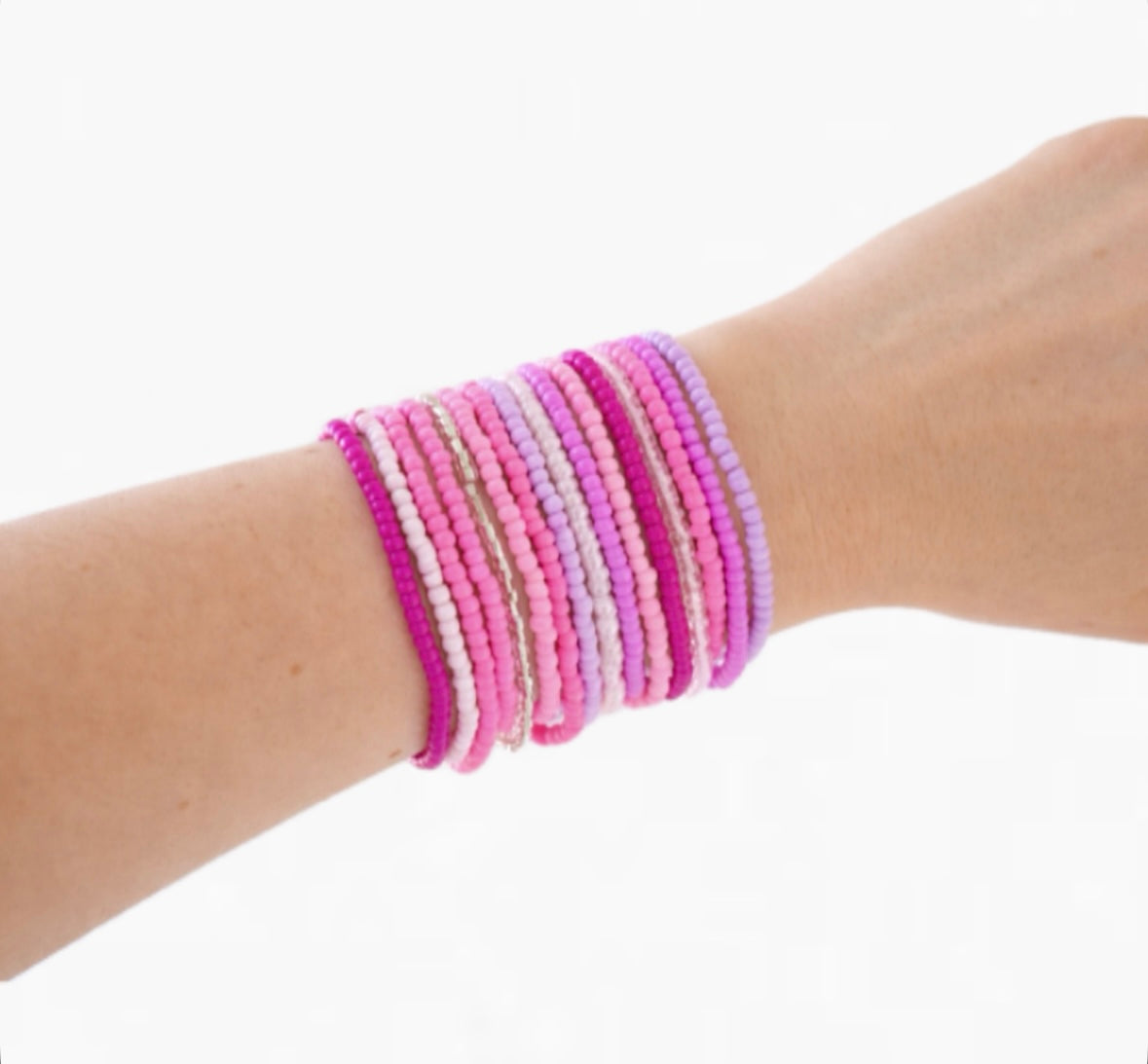 Varying shades of pink beaded bracelets on a wrist against a white background
