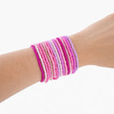 Varying shades of pink beaded bracelets on a wrist against a white background