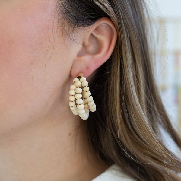 Woman wearing hoops made of three hoops threaded by natural wood beads.