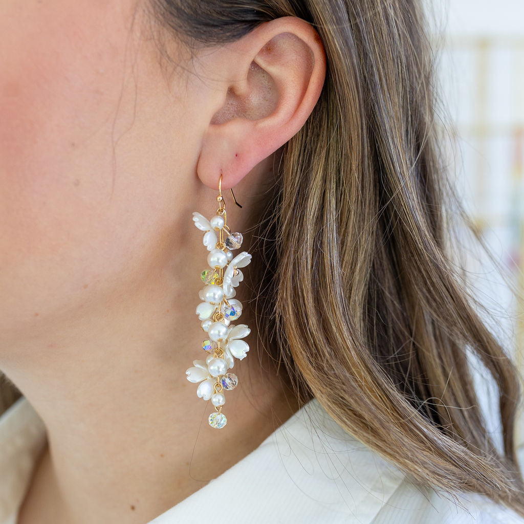 Woman wearing bold, white flower and freshwater Pearl bead dangle earrings.