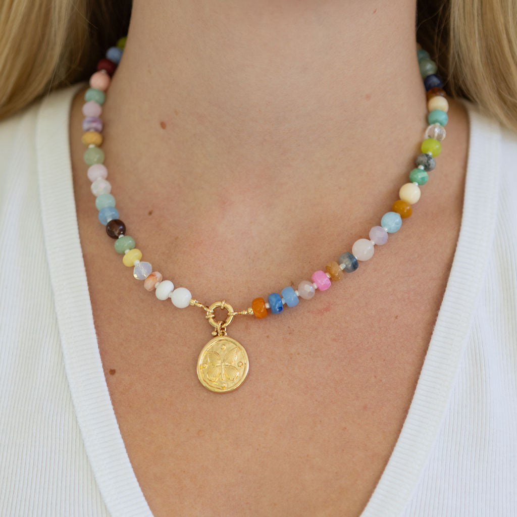 Necklace with multicolored beads with a large central gold clasp and a gold pendant on a person wearing a white top