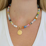 Necklace with multicolored beads with a large central gold clasp and a gold pendant on a person wearing a white top