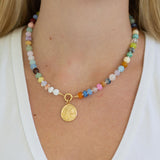 Necklace with multicolored beads with a large central gold clasp and a gold pendant on a person wearing a white top