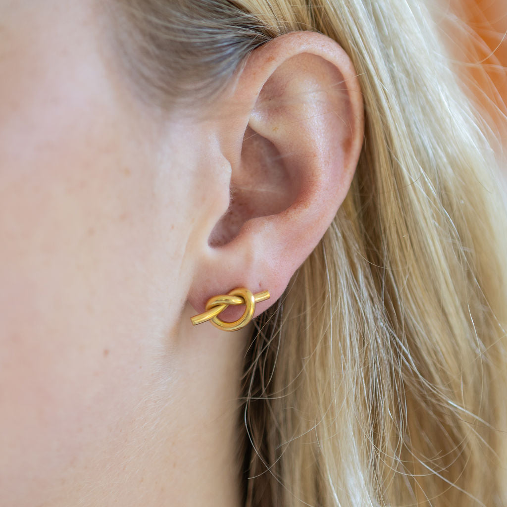 Gold knot earring worn by a person with blonde hair.