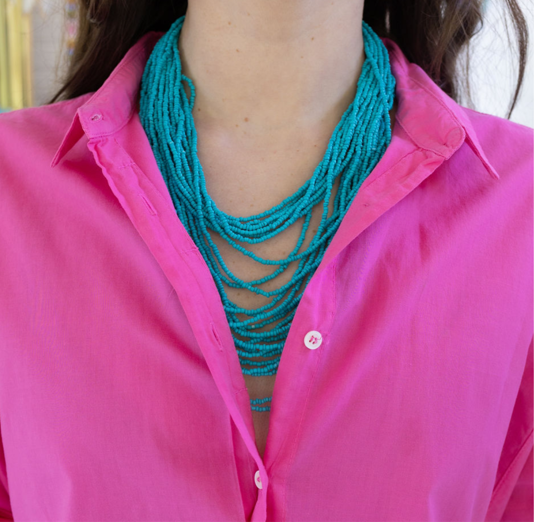 Person wearing a bright pink shirt and multi strand turquoise beaded necklace.